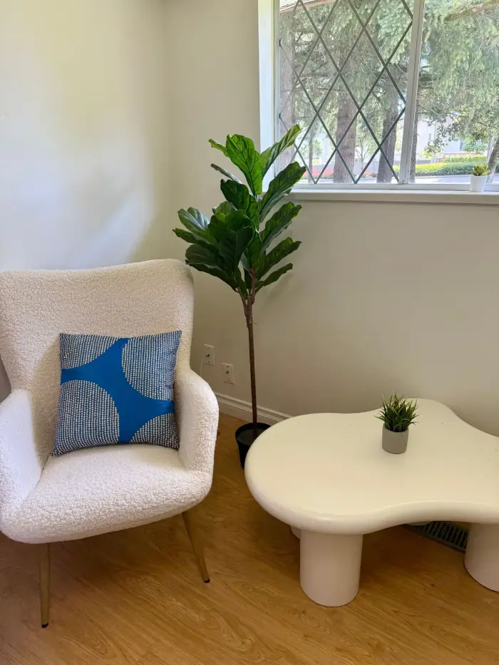 The counselling room at Praxis Wellness in Surrey: a white armchair, a plant and a window onto trees